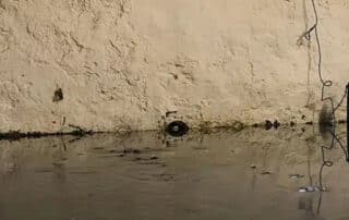 A flooded basement with a drainage pump on the wall, emphasizing the need for basement water cleanup to remove excess water and restore the area.