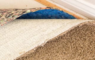 Carpet pulled back to reveal padding and subfloor underneath.