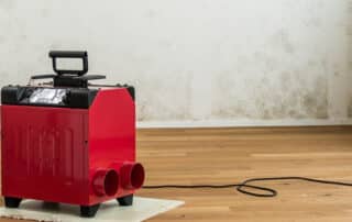 Dehumidifier running in a living room after a water leak, helping dry floors and walls to prevent mold growth.