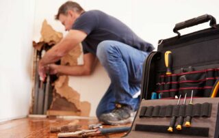 Man repairing wall with tool bag nearby.