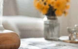 An aroma diffuser on a table with flowers in the background, offering a solution for how to remove smoke smell from the home and restore fresh air.