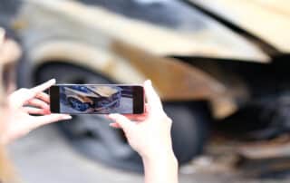 Closeup of female insurance broker taking photos of car after fire accident. The concept of damaged car and insured event