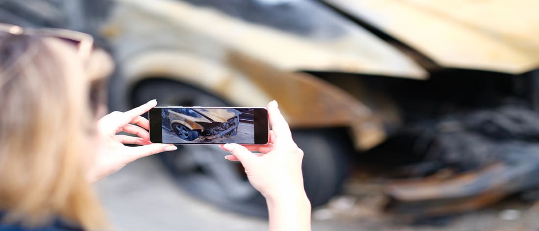 Closeup of female insurance broker taking photos of car after fire accident. The concept of damaged car and insured event