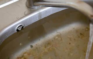 Clogged kitchen sink with food waste and running water. prevent dishwasher flooding