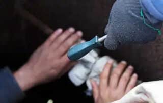 Hands using a tool in a confined space repair, highlighting the importance of sewage remediation to safely address and restore areas affected by sewage damage.