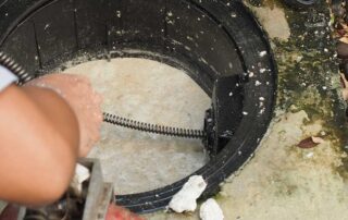 Hand holding drain snake over septic tank