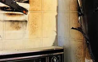 Kitchen fire damage with burnt walls and tiles, highlighting the importance of smoke mitigation to restore and remove smoke damage from the area.