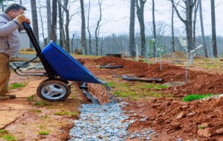 worker uses a wheelbarrow to fill over drainage pipes with crushed stone