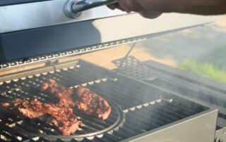 Backyard grill safely positioned away from the house with food cooking, showing fire safety practices to prevent house fires while grilling.