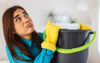 A woman with a mop bucket wearing yellow gloves indoors, emphasizing the need for emergency water damage restoration to quickly address and repair water damage.